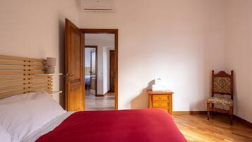A bedroom with a bed, a wooden nightstand, a chair, and a door leading to another room.