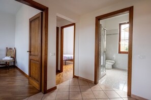 Ein Flur, der zu einem Schlafzimmer mit Bett sowie zu einem Badezimmer mit Dusche und Toilette führt.