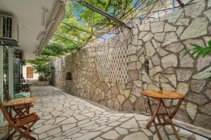 Ein Terrassenbereich im Freien mit Steinboden, einem Holztisch und Stühlen.