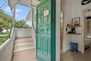 Eine Treppe führt zu einer grünen Tür mit einem Schild, ein kleiner Küchenbereich mit Spüle und Mülleimer sowie ein Bett mit Kopfteil.