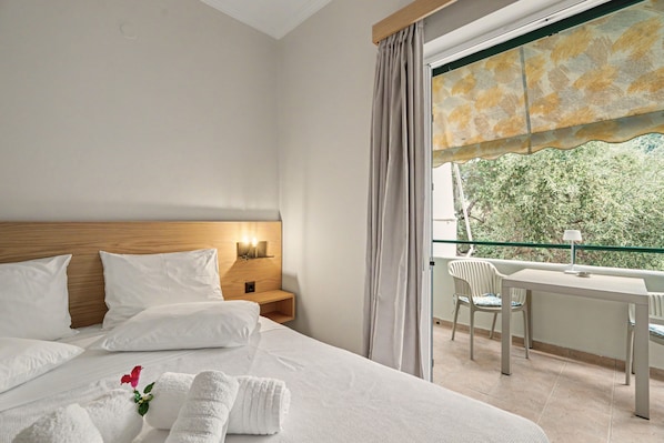 Ein Hotelzimmer mit Bett, Nachttisch und einem Balkon mit Tisch und Stuhl.