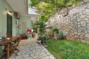 Un espace extérieur aménagé en terrasse, avec un sol en pierre, des meubles en bois et des plantes en pot.
