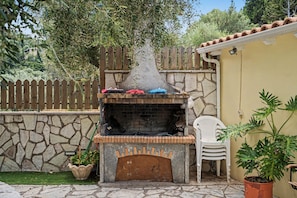 An outdoor brick oven with a chimney, surrounded by a stone wall, a wooden fence, and potted plants. - One Bedroom 11 Apartment with Garden View, Wi-Fi, and Air Conditioning (Lefkada Municipality)