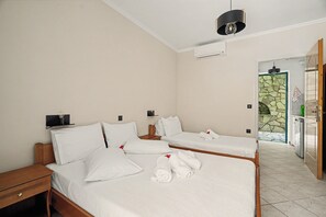 Une chambre d’hôtel avec deux lits simples, une table de chevet en bois, un climatiseur fixé au mur et une porte donnant sur un espace carrelé en pierre.