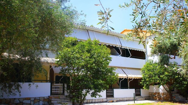 Um edifício de dois andares com uma parede de pedra, uma árvore em primeiro plano e um céu claro.