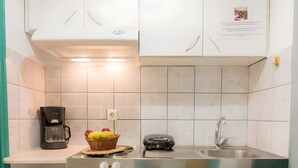 Cozinha compacta com armários brancos, cafeteira, cesta de frutas e pequena geladeira.