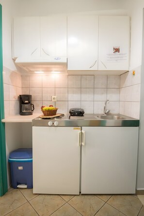 Eine kleine Küche mit weißen Schränken, einer Kaffeemaschine, einem Obstkorb und einem kleinen Kühlschrank.