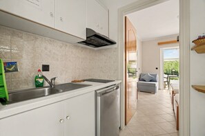 A modern kitchen with a built-in oven, a sink, and a stove. There is a door leading to a dining area with a sofa and a table. - One Bedroom 11 Apartment with Garden View, Wi-Fi, and Air Conditioning (Lefkada Municipality)