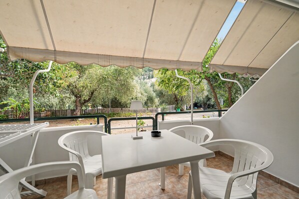Une terrasse avec une table et des chaises, une vue sur les arbres et une clôture, et un sol carrelé.