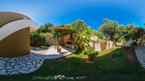 Ein Innenhof mit Steinmauer, einer Pergola und einem Grillbereich.
