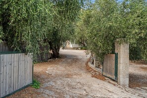 Ein Schotterweg führt zu einem verschlossenen Eingang mit einer Steinmauer und einem Holzzaun.