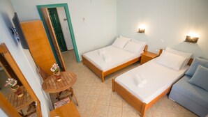Ein Hotelzimmer mit zwei Betten, einem kleinen Tisch mit Stuhl, einer Couch, einem Spiegel und einer Tür.