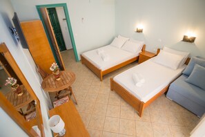 Ein Hotelzimmer mit zwei Betten, einem kleinen Tisch mit Stuhl, einer Couch, einem Spiegel und einer Tür.