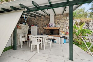 An outdoor patio with a stone wall, a brick fireplace, white plastic furniture, and a ceiling fan. - One Bedroom 9 Apartment with Garden View, Wi-Fi, and Air Conditioning (Lefkada Municipality)