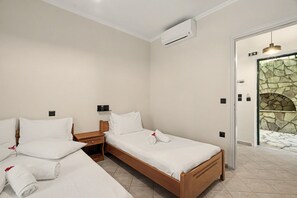 A hotel room with two single beds, a wooden nightstand, a wall-mounted air conditioner, and a stone wall entrance. - One Bedroom 9 Apartment with Garden View, Wi-Fi, and Air Conditioning (Lefkada Municipality)