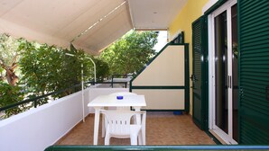 Ein Balkon mit einem weißen Tisch und Stühlen, einer grünen Tür und einem gefliesten Boden.