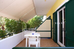 Ein Balkon mit einem weißen Tisch und Stühlen, einer grünen Tür und einem gefliesten Boden.