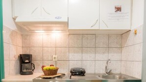Cocina compacta con armarios blancos, cafetera, tostadora y refrigerador pequeño.