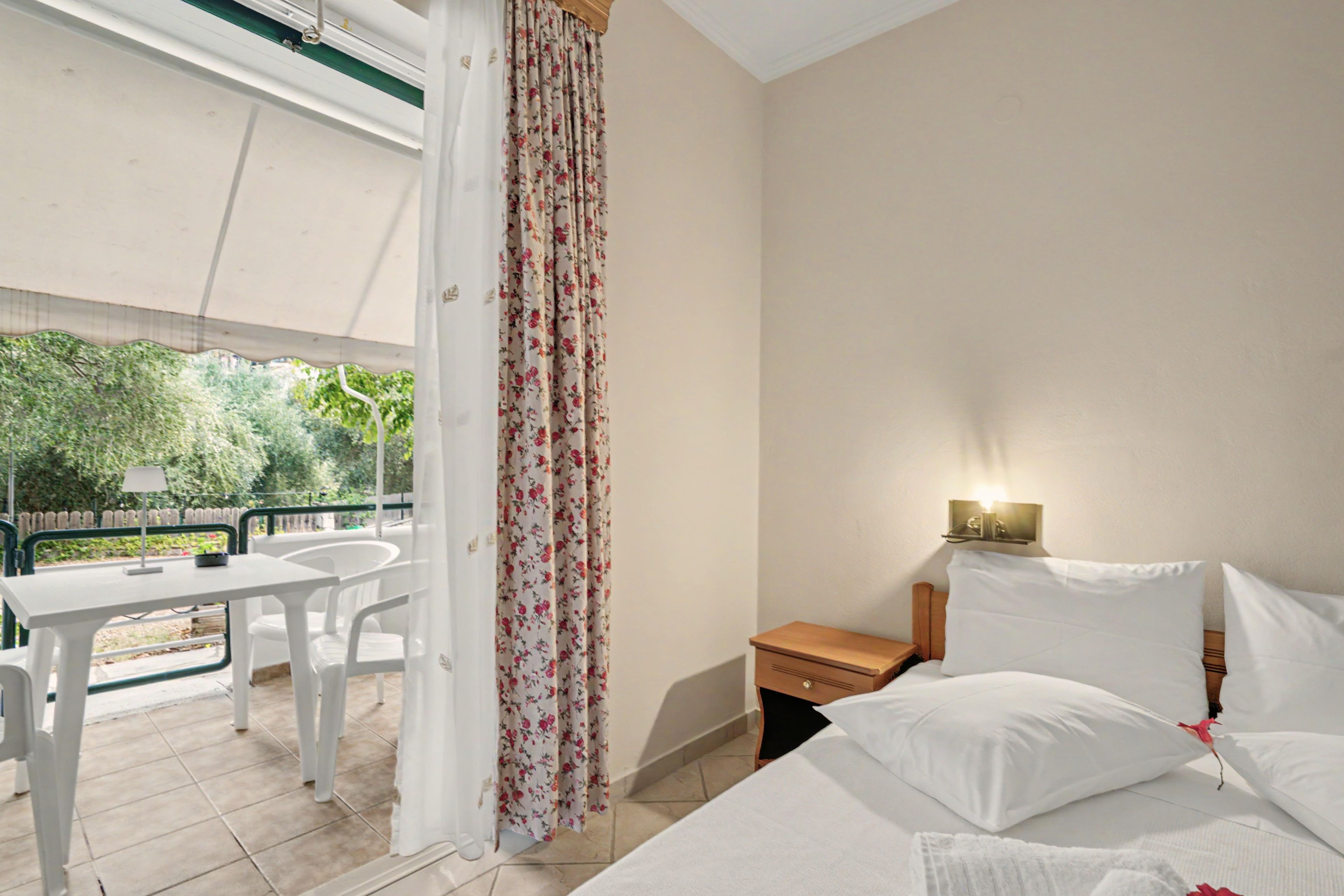 Quarto com cama, mesa de cabeceira, luminária e vista para um jardim pela janela.