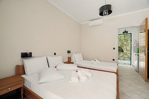 A hotel room with two single beds, a wooden nightstand, a wall-mounted air conditioner, and a door leading to a stone-tiled area. - One Bedroom 8 Apartment with Garden View, Wi-Fi, and Air Conditioning (Lefkada Municipality)