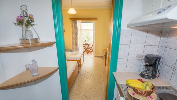 Una habitación de hotel compacta con kitchenette, zona de comedor y vista por una puerta.