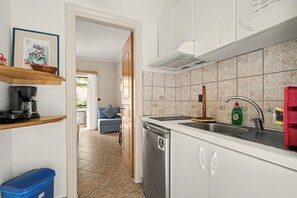 Eine Küche mit weißen Schränken, einer Edelstahl-Spüle und einem Geschirrspüler. Auf der Arbeitsplatte befindet sich ein blauer Mülleimer und ein Korb.