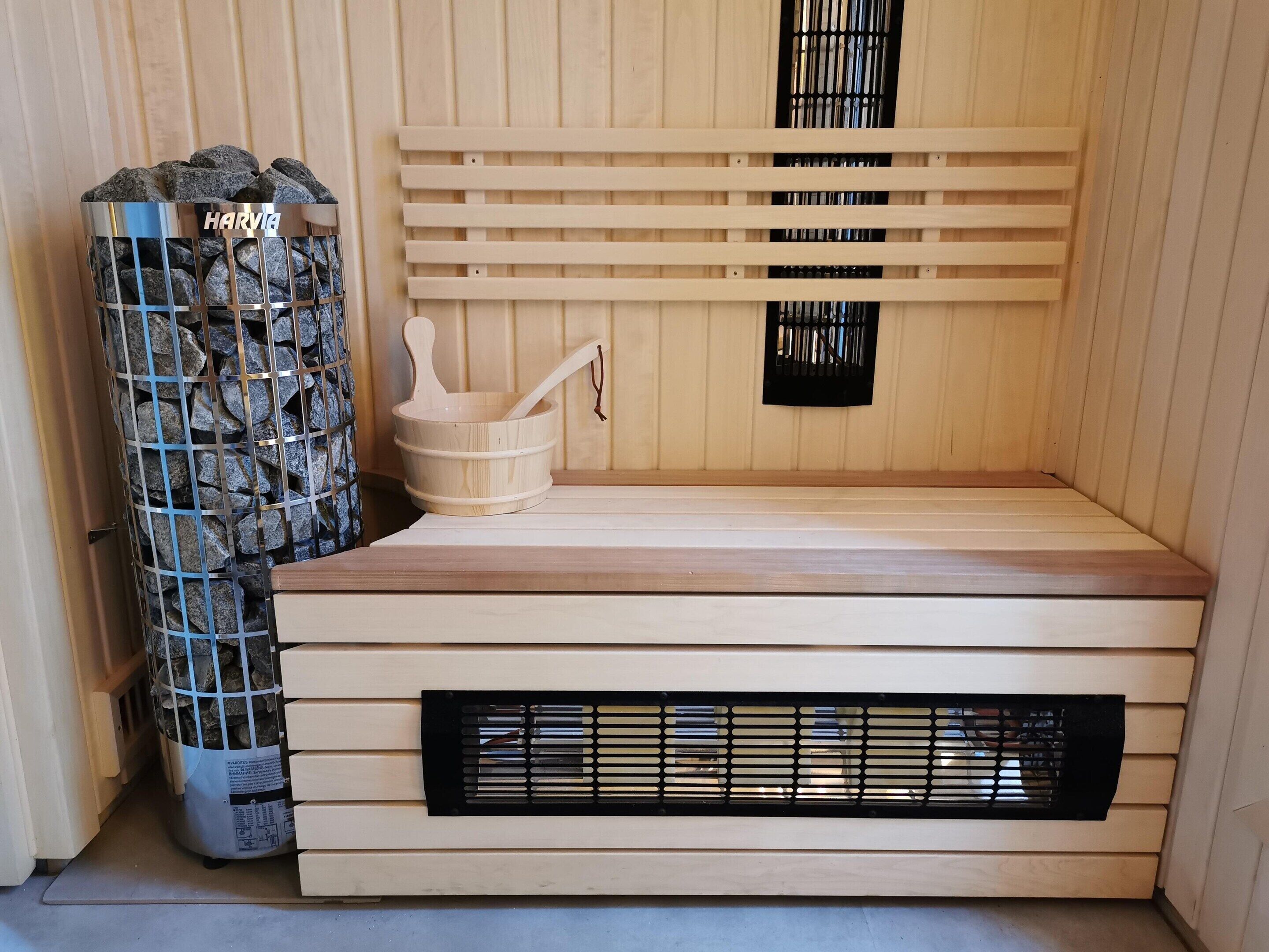 A sauna with a wooden bench, a stone-filled container, and a metal grate.