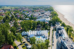 Luftaufnahme einer Küstenstadt mit Strand, Wohngebäuden und einem Schwimmbadbereich.