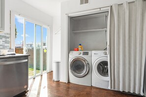 Ein Waschraum mit zwei Waschmaschinen, einem Mülleimer und einem Fenster mit Außenblick.