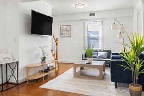Ein modernes Wohnzimmer mit Flachbildfernseher, einer Couch, einem Couchtisch und Topfpflanzen.