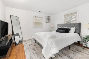 Un dormitorio con una cama, televisor, espejo y ventana con persianas.