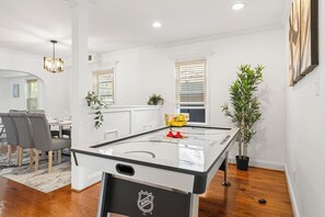 Ein modernes Wohnzimmer mit einem Kicker, einer Essecke mit Stühlen und einer Topfpflanze.
