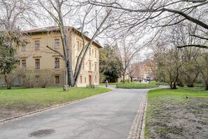 Ein gepflasterter Weg führt zu einem Gebäude mit vielen Fenstern und einem zentralen Eingang.