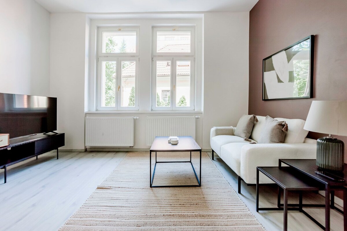 A modern living room with a sofa, a coffee table, a TV, and a large window with a view of buildings.
