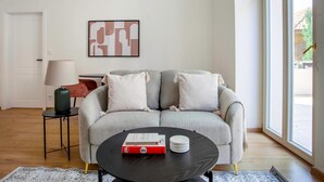 Uma sala de estar com um sofá cinzento, uma mesa de centro preta, uma luminária e uma obra de arte abstrata emoldurada na parede.