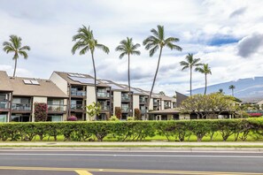 A multi-story residential building with balconies, solar panels, and a well-maintained garden with palm trees. - Beautiful 1 Bedroom / 1 Bath on the ground floor at popular Hale Kamaole. (Kihei)
