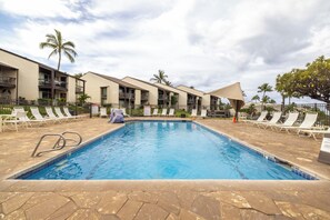 A swimming pool with lounge chairs and a covered area, surrounded by a building with balconies. - Beautiful 1 Bedroom / 1 Bath on the ground floor at popular Hale Kamaole. (Kihei)