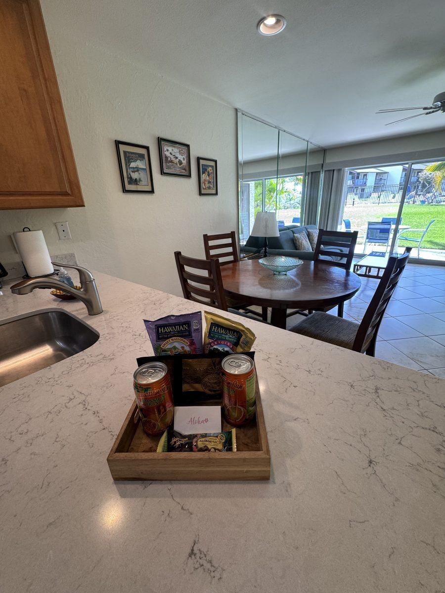 A kitchen with a marble countertop, a wooden dining table, and chairs. There is a window with a view of the outdoors.