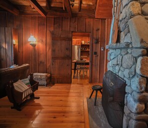 Ein Holzinterieur mit Kamin aus Stein, Holzboden und einem durchgehenden offenen Durchgang zur Küche.