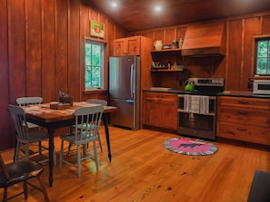 Ein Interieur einer Holzhütte mit Esstisch, Stühlen, einem Kühlschrank, einer Mikrowelle und einem Herd.