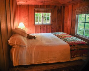 A wooden cabin bedroom with a bed, a window, and a lamp. - Historic 3-BR cottage on coveted Megunticook Lake with AC/heat in Camden ME. (Camden)