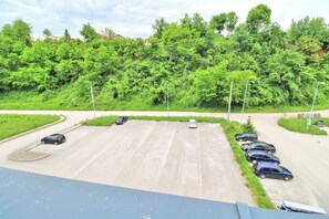 A parking lot with cars, a road curving to the left, and a dense green forest in the background. - Apartman Slani San Tuzla – Modern Apartment with Free Parking (Tuzla Grad)
