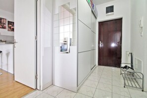 A hallway with a wooden door, a white wall with a small window, and a tiled floor.