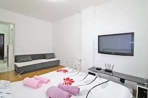 A modern hotel room with a bed, a sofa, a TV, and a desk with a computer.