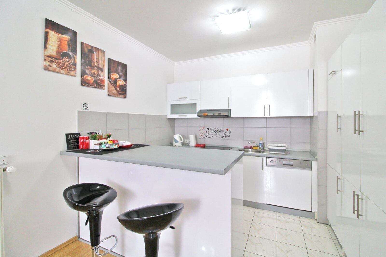 A modern kitchen with white cabinets, a central island with stools, a microwave, and a coffee machine.
