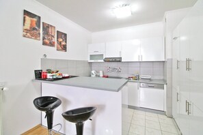 A modern kitchen with white cabinets, a central island with stools, a microwave, and a coffee machine.