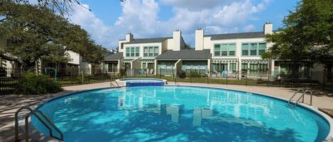 A swimming pool with a wooden deck, surrounded by a fence and trees.