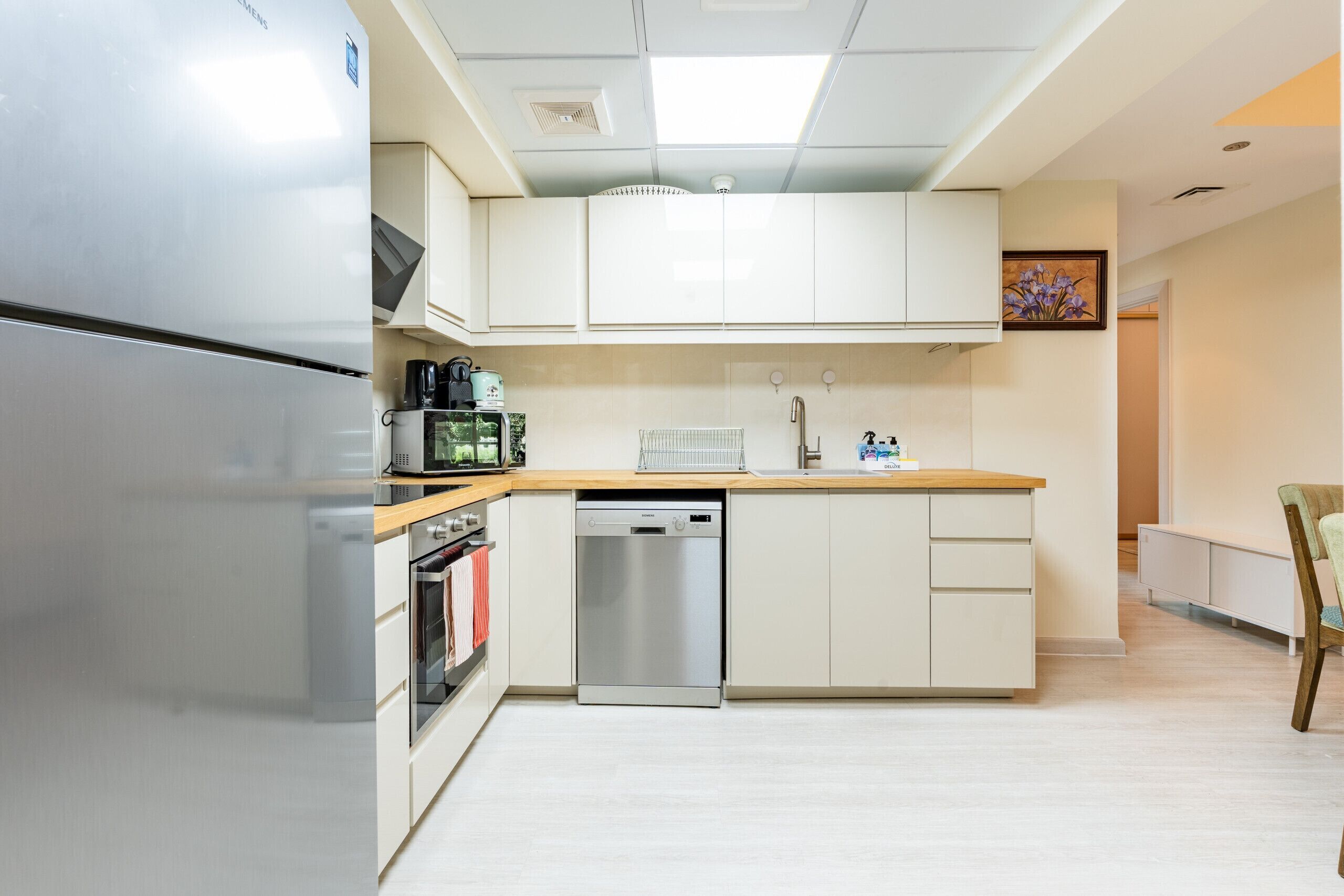 Una cocina moderna con un refrigerador de acero inoxidable, horno empotrado, lavavajillas y cafetera.
