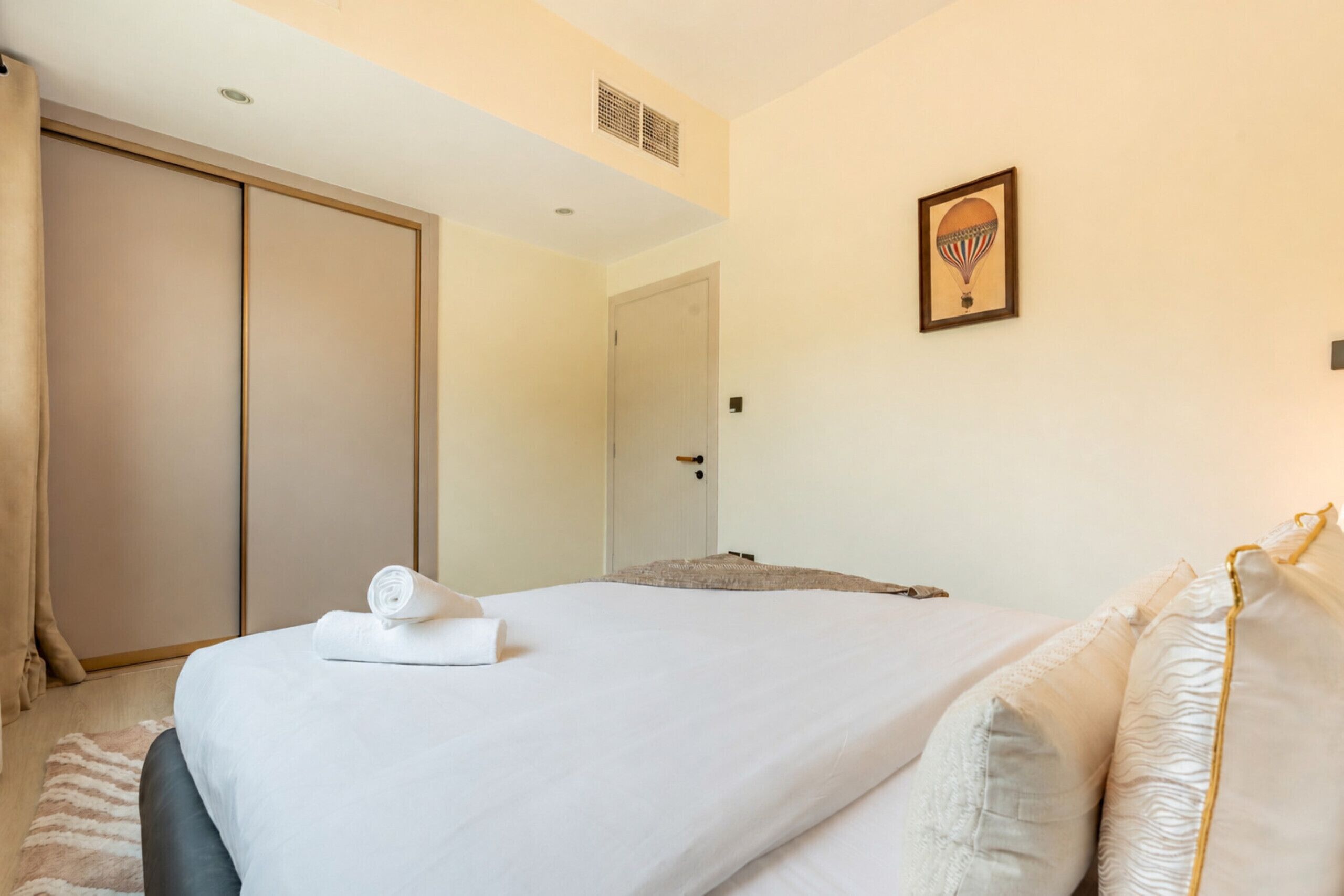 A hotel room with a bed, a door, a framed picture on the wall, and a towel on the bed.