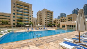 A swimming pool with lounge chairs and umbrellas, surrounded by multi-story buildings. - Quiet 2BR Haven Steps from The Greens Lakes and Emirates Golf Club,Al Dhafrah 2 (Dubai)
